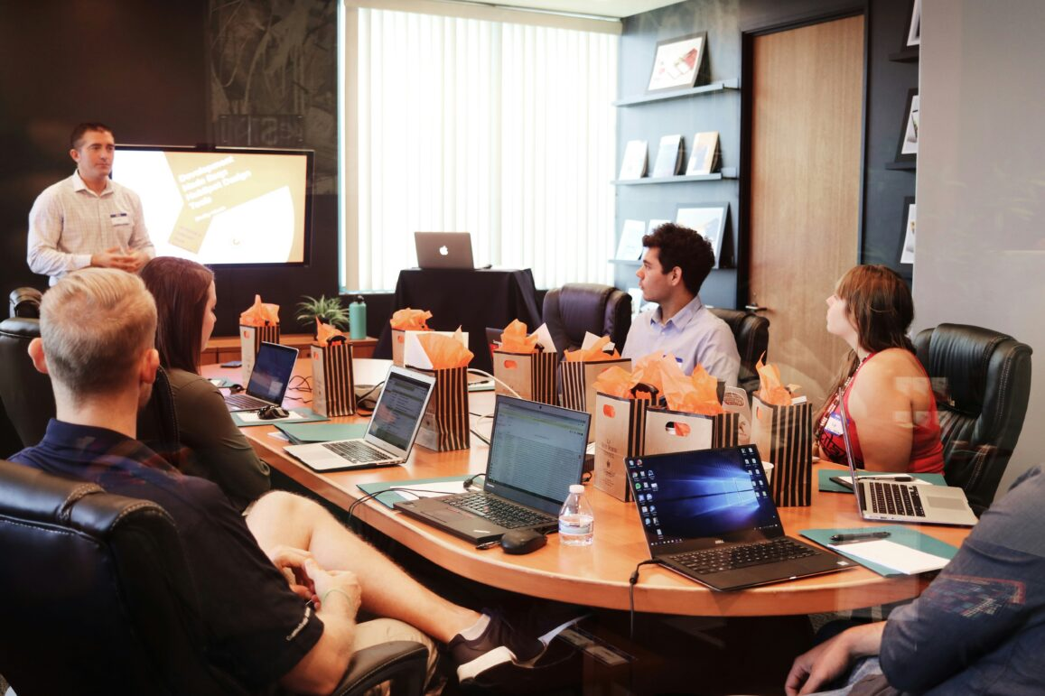 A presenter speaks to attendees gathered around a conference table during a meeting.